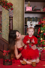 Christmas family scene of love and fairy. Mother holding cute baby girl daughter by hands close to new year tree.