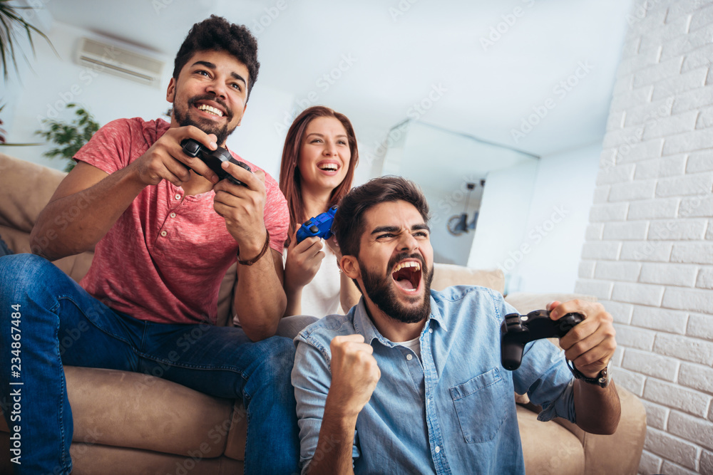 Wall mural group of young friends play video games together at home.