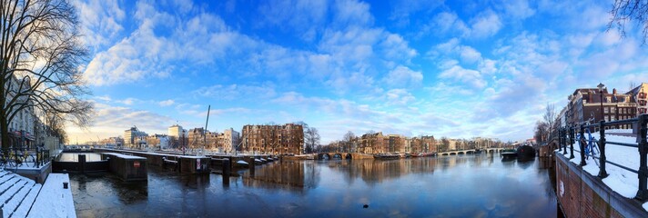 Beautiful 180 degree cityscape panorama of the river Amstel in Amsterdam, the Netherlands, in winter with ice and snow with the famous skinny bridge (magere brug)
