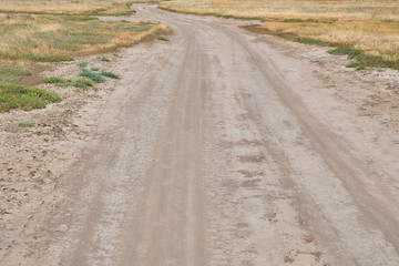 Rural dirty dusty and winding road crossing the steppe with drying grass