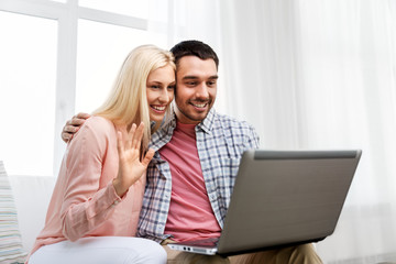 technology, internet and people concept - smiling happy couple with laptop computer having video call at home