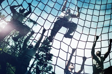 Military soldiers climbing rope during obstacle course