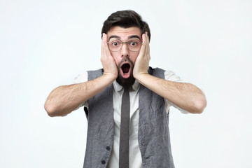 Emotional scared brunet male looks with frightened expression as sees something awful in front,...