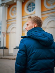 The man is blond with short hair, in a winter jacket stands with his back to the camera and looks at the beautiful old Church with yellow stucco facades