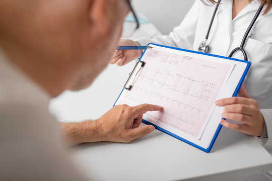 medicine, age, health care, cardiology and people concept - close up of senior man and doctor with cardiogram on clipboard at hospital