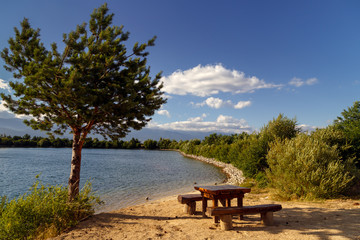 Fototapeta na wymiar Picnic place on the sand shore of beautiful lake, pine tree, summer sunny day. Place for recreation. Calm and tranquility.