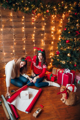 Fototapeta na wymiar Friends wrapping and decorating gift near Christmas tree