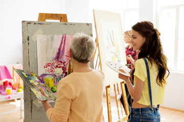 creativity, education and people concept - happy women with brushes and palettes painting still...