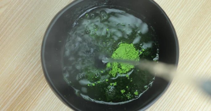 Pouring water and mixing matcha tea in bowl