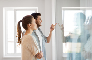 mortgage, people and real estate concept - happy couple looking through window at new home