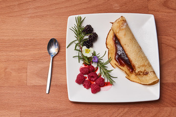 Plate with pancake and fruit on a wooden table top.