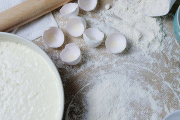 Table with ingredients for dough, broken eggs, flour, mold for cake and rolling pin. Process of preparing pie, kitchen objects, flat lay with light white and blue colors space for text
