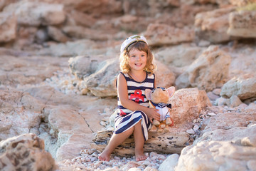 Beach cute girl posing on a rocky beach barefooted with curly hair wearing sailor dress and sun glasses.