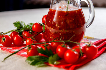 Fresh homemade tomato juice in a glass jar and fresh tomatoes on a table with celery leaves