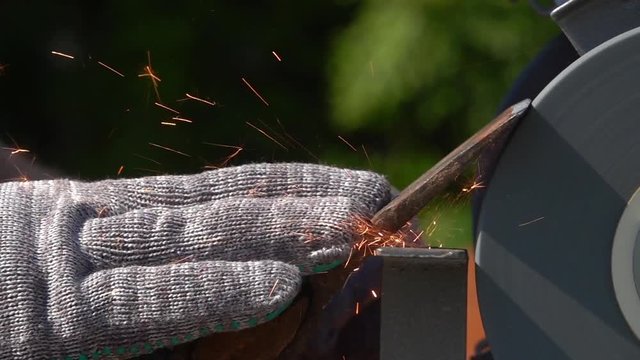 Sharpening of old grange ax with unbalanced grinding machine in slow motion close up. Panning of traditional machinery scene with retro tool, waving hand in safety glove and turning grindstone wheel.