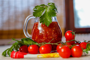 Fresh homemade tomato juice in a glass jar and fresh tomatoes on a table with celery leaves