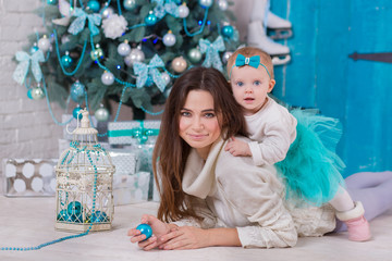 Christmas family at homely cozy house posing close to new-year tree colored in blue. Beautiful woman with cute baby daughter in scene of winter holiday tender love.