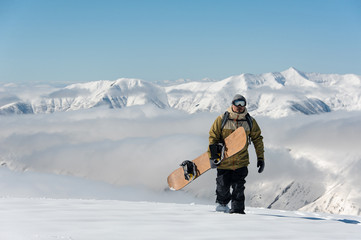Fototapeta na wymiar Manful snowboarder walking with the brown snowboard in the mountain resort