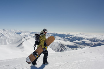 Side view manful snowboarder walking with the snowboard in the mountain resort