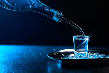 Crédence de cuisine en verre imprimé Bar Vodka poured into a glass lit with blue backlight.