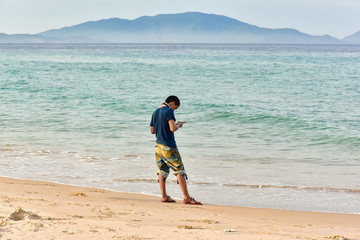 Lonely man stands on beach by sea and uses smartphone