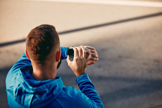Close up of sporty bearded man kneeling and setting stopwatch. Healthy lifestyle concept.