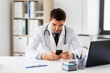 Fototapeta na wymiar healthcare, medicine and technology concept - male doctor with smartphone at medical office in hospital