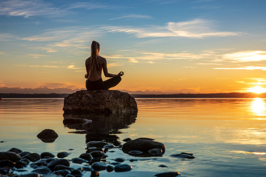 hübsche junge frau macht yoga auf einem Stein im Wasser See Meer im Sonnenuntergang Abendrot
