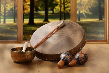 A still life of the shamanic drum, Tibetan singing bowls and maracas on a background of forest.