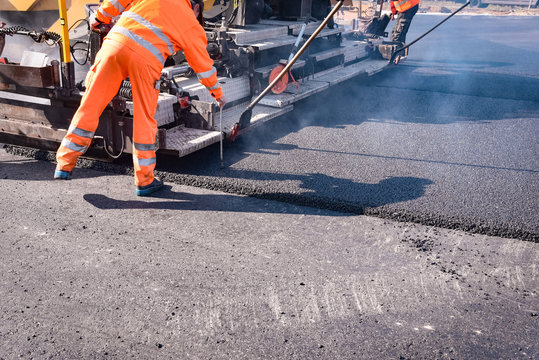 Stra&szlig;enbau - neue Asphaltdecke wird gezogen, Arbeiter misst die Schichtdicke