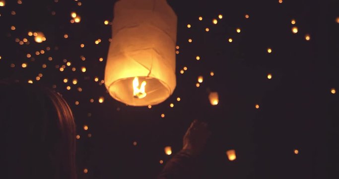 Happy young woman releasing lit paper lantern at night  during lantern festival 