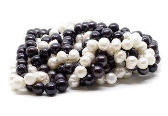 Two strands of white and black pearls intertwined on white background isolated