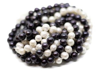 Two strands of white and black pearls intertwined on white background isolated