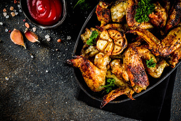 Baked grilled chicken wings on a black plate, with spices and ketchup sauce, on dark concrete background. Top view copy space