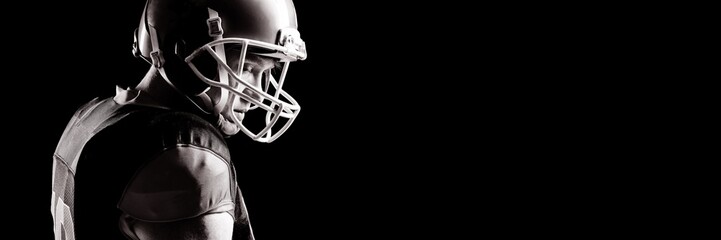 American football player in helmet standing against black