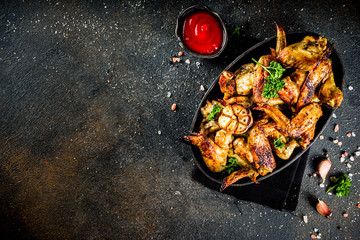 Baked grilled chicken wings on a black plate, with spices and ketchup sauce, on dark concrete background. Top view copy space