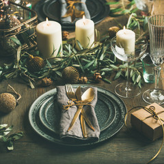 Christmas or New Years party table setting. Plates, golden cutlery, glasses, gift box, festive branch decoration, candles, gliterring toys over wooden table background, selective focus, square crop