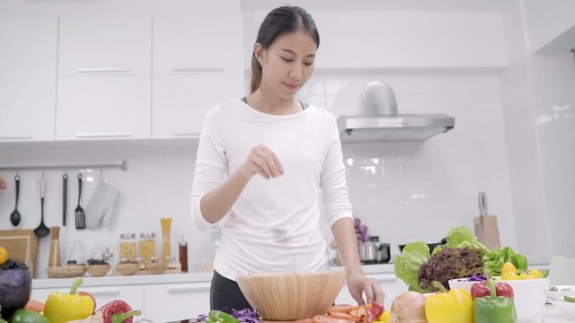 Young Asian woman making salad healthy food in the kitchen, beautiful female in casual use organic vegetables lots of nutrition preparing salad for fit body at home. Healthy food concept.