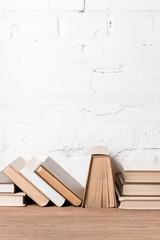 books with hardcovers on wooden table near white brick wall