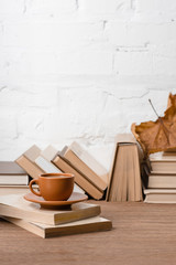 books, cup of coffee and dry autumn leaf on wooden table