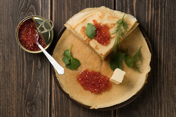 Top view of yummy pancakes decorated with red salmon caviar, cilantro, dill and piece of butter on...