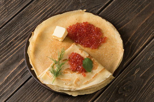 Pancakes with red salmon caviar on wooden background