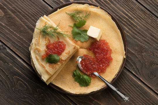 Flat lay of pancakes with red caviar decorated with green leaves of cilantro and dill