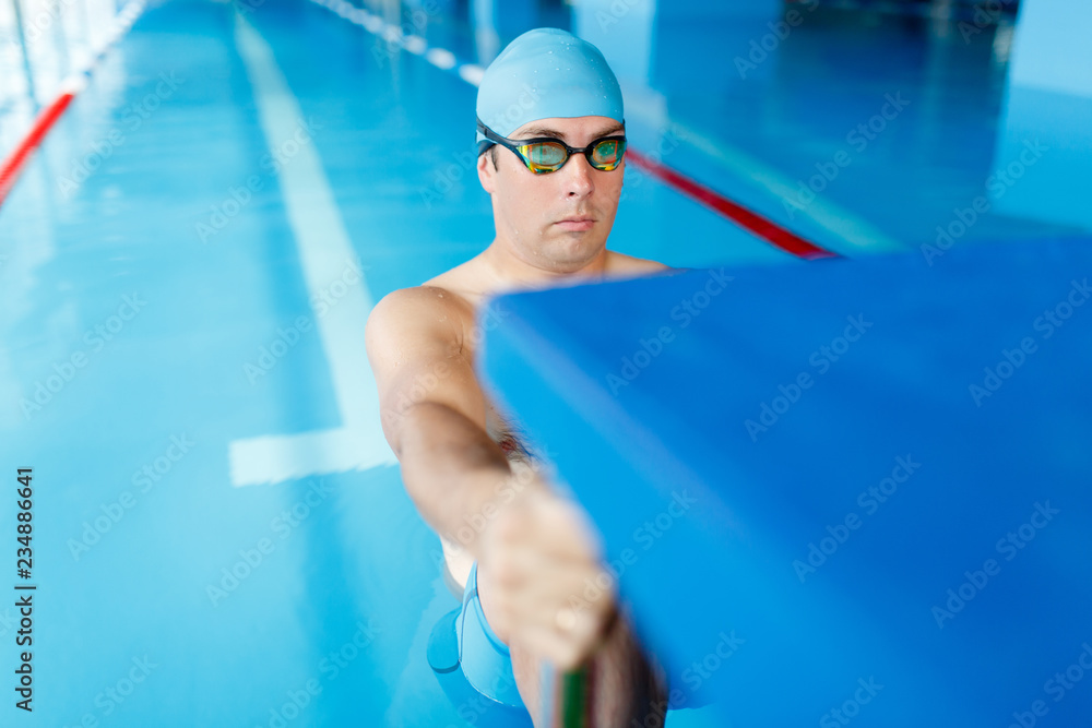 Wall mural Photo of sportive swimmer man in blue cap at side in swimming pool during training