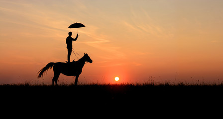 Horsemanship and trick-riding scene: men, standing on horse with open umbrella.  Romantic scene on idyllic sunset. 