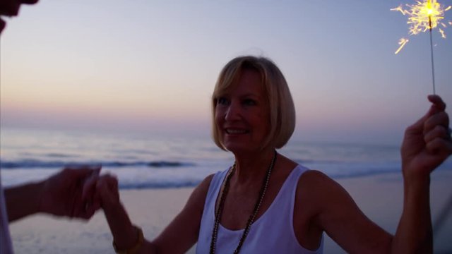 Happy Caucasian seniors dancing with sparklers on the beach at sunset