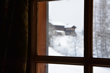 View through a hut window with winter, snow ad some huts outside