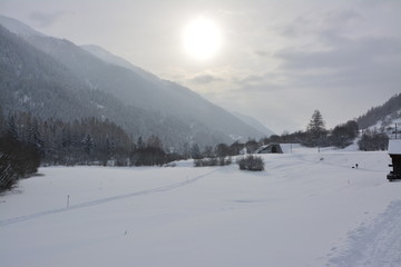 Sunny winter landscape in swiss mountains with some huts in the background