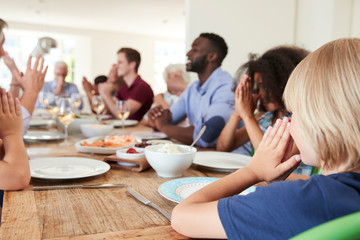 Obraz premium Multi-Generation Family And Friends Around Table Praying Before Meal At Party