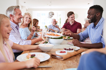 Group Of Multi-Generation Family And Friends Sitting Around Table And Enjoying Meal